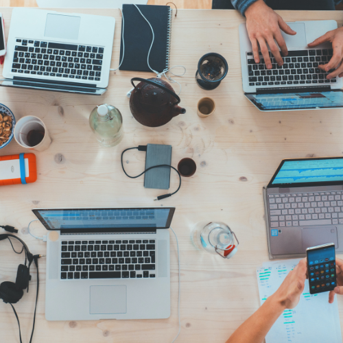 A picture of four laptops on the table with power bank and coffee. 